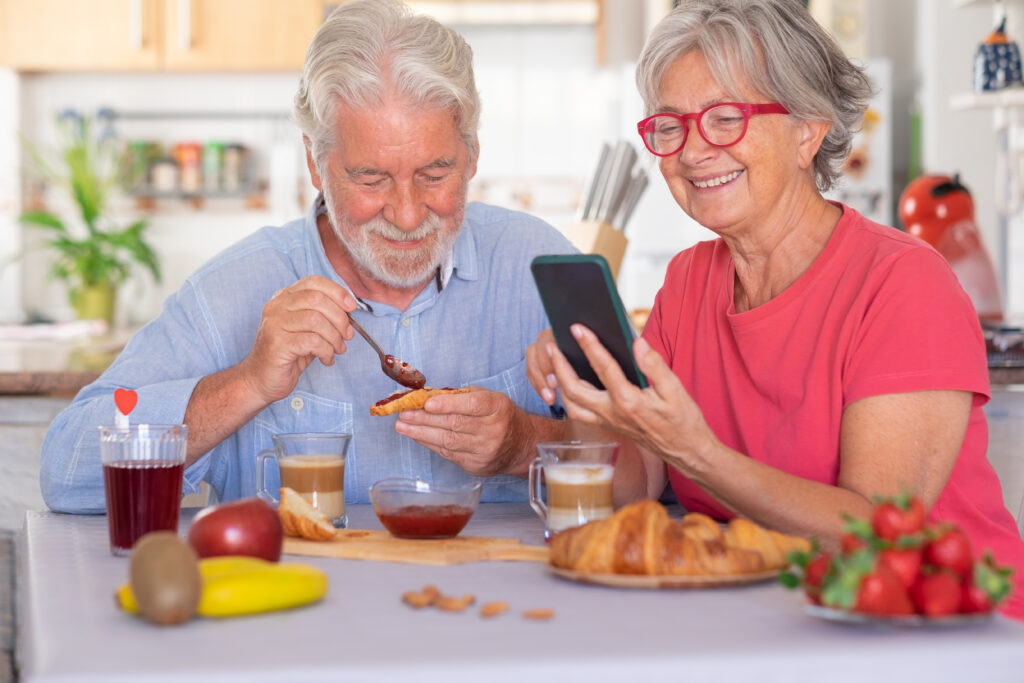 Smiling older couple at breakfast using a phone to track their meal